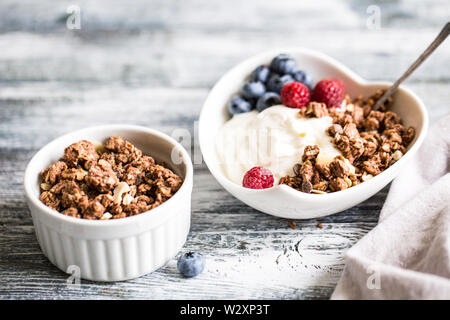 Greek yogurt, blueberries, raspberries and granola in a white bowl on a wooden background. Stock Photo