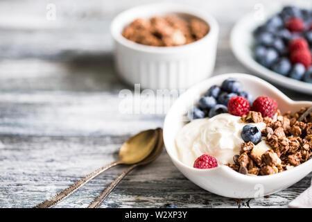 Greek yogurt, blueberries, raspberries and granola in a white bowl on a wooden background.