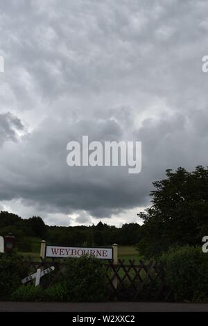 dark grey clouds over the station name sign at Weybourne station on the North Norfolk railway Stock Photo
