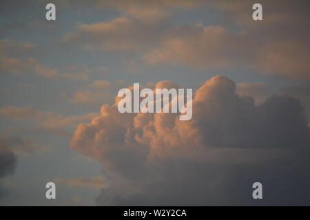 Billowing cummulus  white fluffy clouds catching the light of the evening sun setting, glowing at the edges Stock Photo