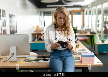 Female graphic designer reviewing photos on digital camera at desk Stock Photo