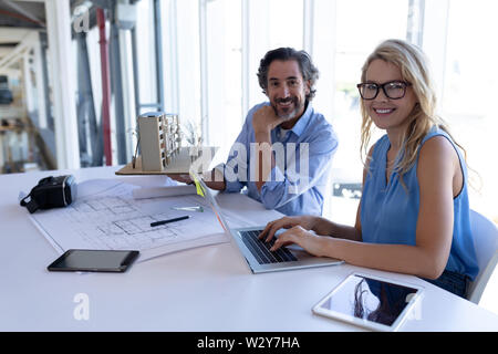 Male and female architect looking at camera while working table in a modern office Stock Photo