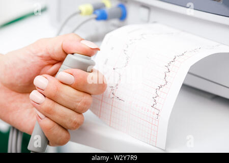 Close-up shot of pregnant woman's hand holding controller of the Cardiotocograph machine aka Electronic Fetal Monitor (EFM) recording the fetal heartb Stock Photo