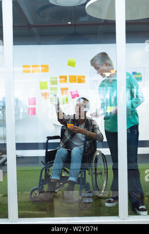 Male and female executives discussing over sticky notes in office Stock Photo