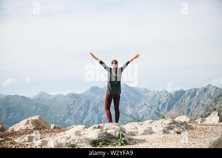 Girl on top of a mountain or hill raises his hands up. She's happy and free. Stock Photo