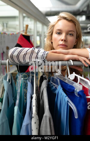 Female fashion designer leaning on clothes rack in design studio Stock Photo