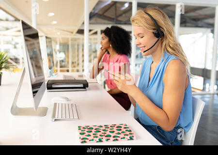 Female customer service executive using mobile phone at desk Stock Photo