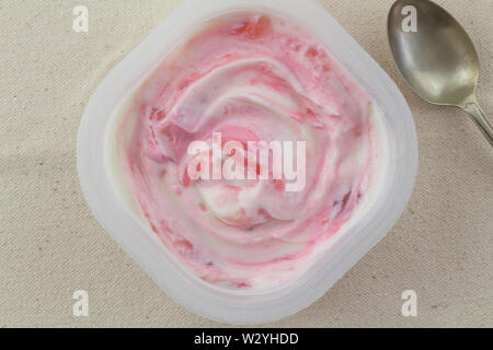 Yogurt cup with natural strawberry greek white and pink  yogurt swirled with real strawberries isolated on rustic linen background with small silver s Stock Photo