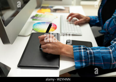 Female graphic designer using graphic tablet at desk in office Stock Photo