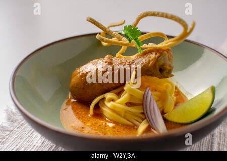 thai yellow chicken drumsticks curry with fresh egg noodles , lime, coriander and crispy fried egg noodles in a plated dish Stock Photo