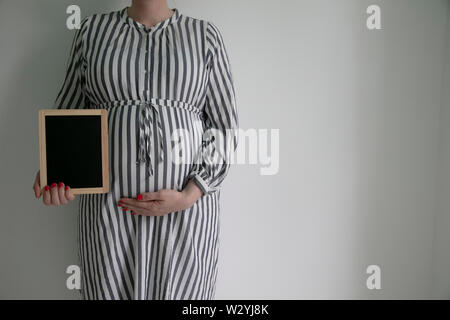 A pregnant woman holding a blak chalkboard near her pregnant belly Stock Photo
