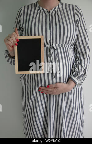 A pregnant woman holding a blak chalkboard near her pregnant belly Stock Photo