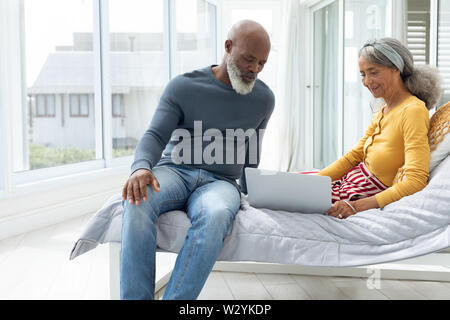 Couple sitting on a bed while using a laptop Stock Photo