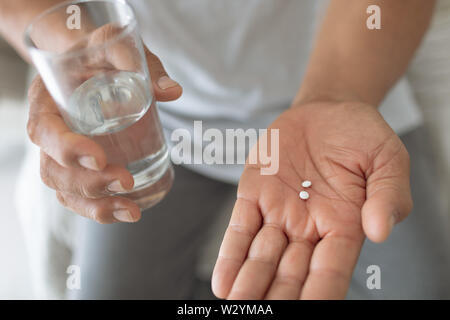 Man sitting on the bed while holding pills and a glass of water Stock Photo