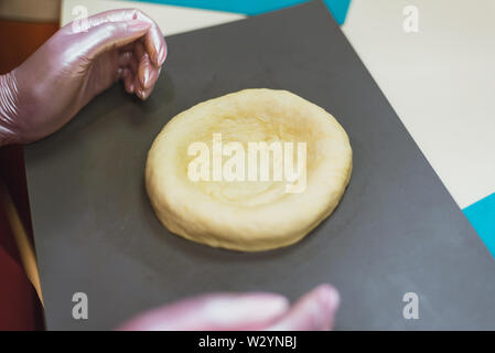 sculpt from dough buns and bread. the woman kneads the dough and makes round bread from it. A cook in gloves creates a tasty bakery product. Stock Photo