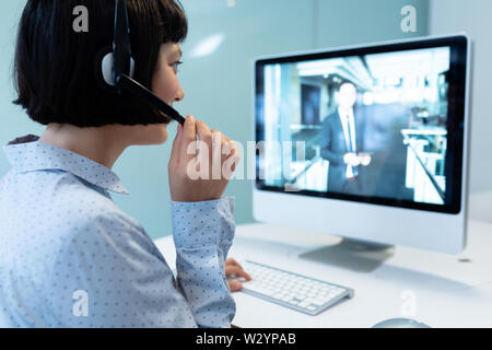 Asian Female customer service executive making video call on computer at desk Stock Photo