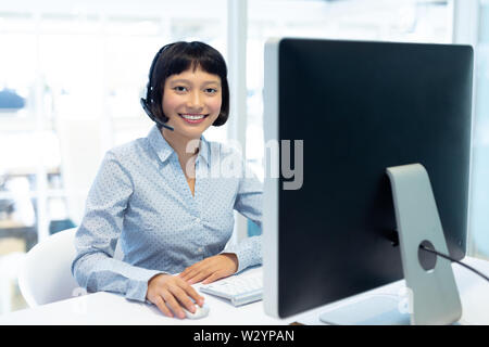 Asian Female customer service executive working on computer at desk Stock Photo