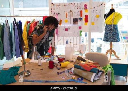 Male fashion designer talking on mobile phone while working on a table Stock Photo