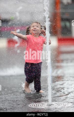 Birmingham, UK. 11th July, 2019. Two-year-old Orla from Coventry delights in the new fountains in Birmingham’s Centenary Square. With £16m already spent on the redevelopment of the square as well as further millions spent on the city centre modernisation, the famous Symphony Hall is also earmarked for changes. [Parental Consent given] Peter Lopeman/Alamy Live News Stock Photo