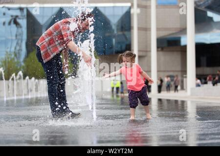 Birmingham, UK. 11th July, 2019. Two-year-old Orla from Coventry delights in the new fountains in Birmingham’s Centenary Square. With £16m already spent on the redevelopment of the square as well as further millions spent on the city centre modernisation, the famous Symphony Hall is also earmarked for changes. [Parental Consent given] Peter Lopeman/Alamy Live News Stock Photo