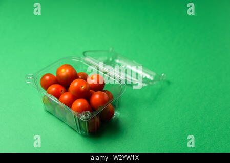 Fresh cherry tomatoes in plastic package. Zero waste, recycle concept. Plastic pollution. Green background Stock Photo
