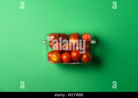 Fresh cherry tomatoes in plastic package. Zero waste, recycle concept. Plastic pollution. Green background Stock Photo
