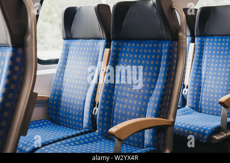 Rows of blue fabric seats with leather headrests inside empty modern train, travel concept, selective focus. Stock Photo