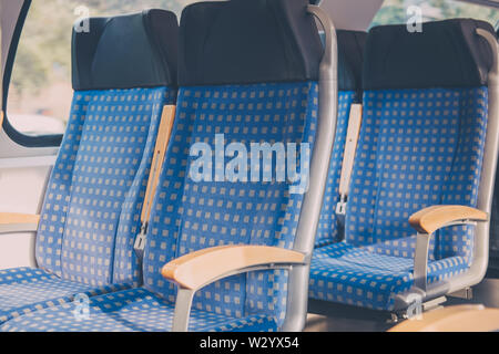 Rows of blue fabric seats with leather headrests inside empty modern train, travel concept, selective focus. Stock Photo