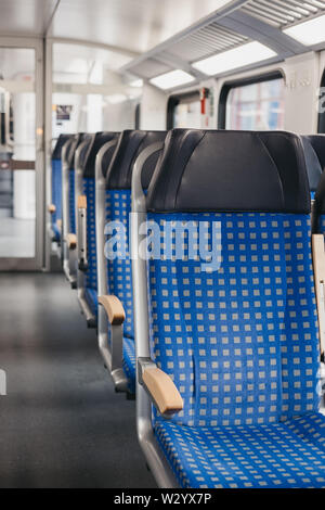 Rows of blue fabric seats with leather headrests on one side of an aisle inside empty modern train, travel concept, selective focus. Stock Photo