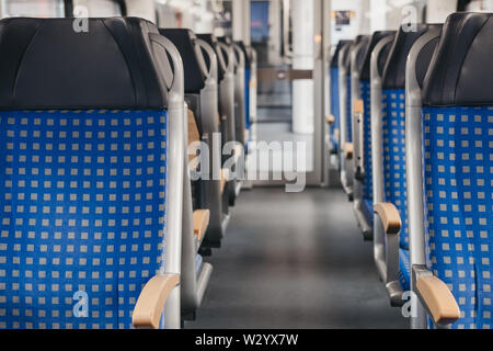 Rows of blue fabric seats with leather headrests on both sides of an aisle inside empty modern train, travel concept, selective focus. Stock Photo