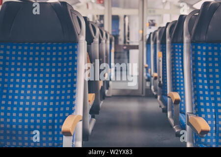 Rows of blue fabric seats with leather headrests on both sides of an aisle inside empty modern train, travel concept, selective focus. Stock Photo