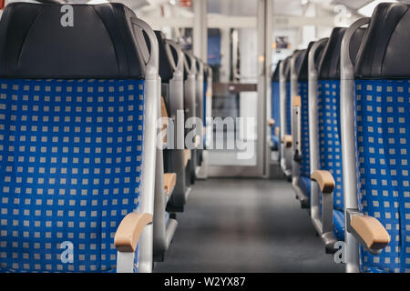 Rows of blue fabric seats with leather headrests on both sides of an aisle inside empty modern train, travel concept, selective focus. Stock Photo