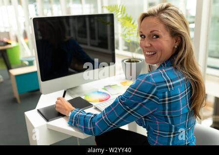 Female graphic designer using graphic tablet at desk in office Stock Photo