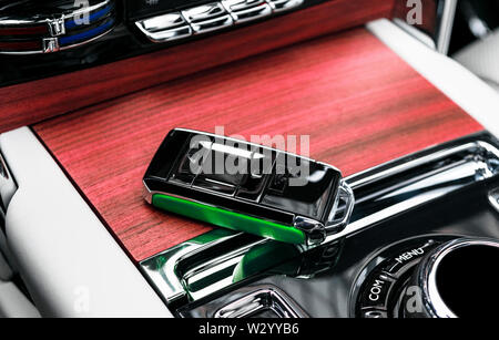 Closeup inside vehicle of wireless green leather key ignition on natural wood panel. Wireless start engine key. Car key remote isolated. Modern Car ke Stock Photo