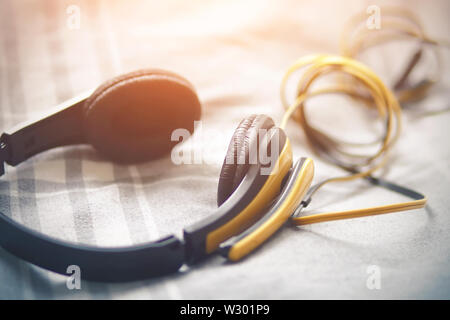 Yellow large headphones with microphone and long tangled wire lying on a soft grey blanket with white stripes, illuminated bright orange sunlight. Stock Photo