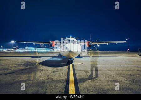Starting of engines of turboprop airplane before take off against airport at night (long exposure). Stock Photo
