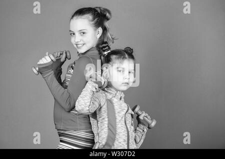 Sport exercises for kids. Healthy upbringing. Sporty babies. Following her sister. Girls cute kid exercising with dumbbells. Motivation and sport example concept. Toddler repeat exercise after sister. Stock Photo