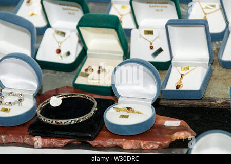 A shop display case of earrings, necklaces and rings with various local cut precious gems and sapphires in a Gem shop in  Sapphire, a small town in th Stock Photo