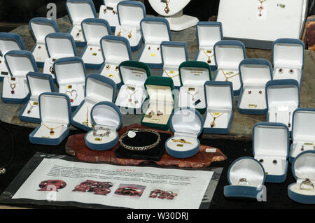 A shop display case of earrings, necklaces and rings with various local cut precious gems and sapphires in a Gem shop in  Sapphire, a small town in th Stock Photo