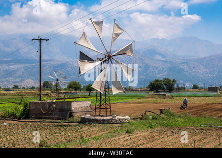 Greek farmer working in field with traditional windmills on Lasithi Plateau, Crete, Greece Stock Photo