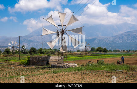 Greek farmer working in field with traditional windmills on Lasithi Plateau, Crete, Greece Stock Photo