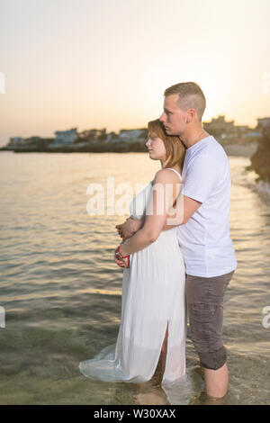 Pregnant woman embracing with her husband on the beach at sunset Stock Photo