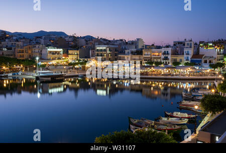 Fishing boats moored along Lake Voulismeni in Agio Nikolaos in evening, Crete, Greece Stock Photo