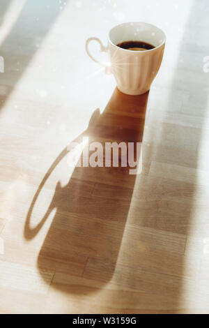 Coffee white cup standing on wooden table with long shadow side view. Breakfast tea image. Good morning concept. Mug with hot drink, espresso beverage Stock Photo