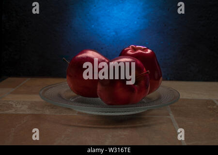 three red and shiny apples with rim light on top with dark blue background on a table, as dark food photography Stock Photo