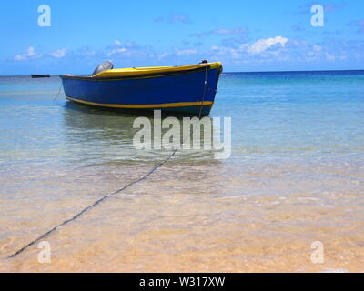 Blue speedboat (dinghy) with yellow trim and a single outboard engine moored in the shallows, Crocus Bay, Anguilla, BWI. Stock Photo