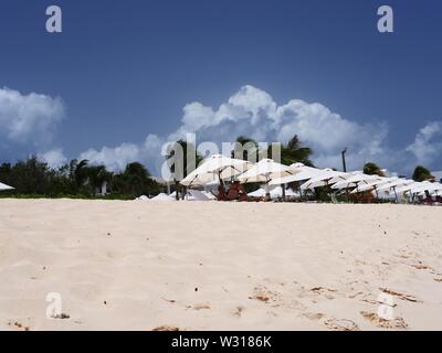 Blinding white sand leading up to white sunshades and towering clouds and and palm trees, Meads Bay, Anguilla, BWI. Stock Photo