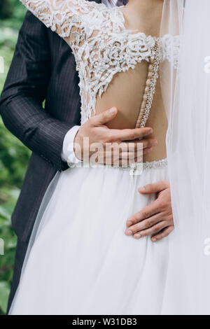 Rear view of bride in a white dress and groom hugs, blurred green background. First wedding dance concept Stock Photo