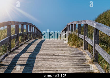 A wooden pathway crossing the dunes. The way leads to the beach on a beautiful summer day. Stock Photo