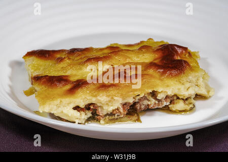 Greek moussaka dish recipe preparation. Ready meal closeup on white dish served portion of baked mousaka with bechamel potatoes above ground beef meat Stock Photo